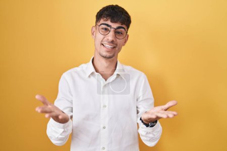 Téléchargez les photos : Jeune homme hispanique debout sur fond jaune souriant joyeuse offrant des mains donnant assistance et acceptation. - en image libre de droit