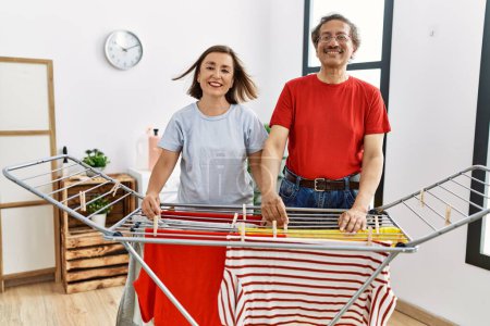 Foto de Mediana edad hombre y mujer pareja sonriendo confiado colgando ropa en tendedero en la lavandería - Imagen libre de derechos