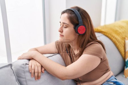 Young woman listening to music sitting on sofa at home