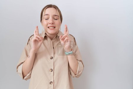 Téléchargez les photos : Jeune femme caucasienne portant une chemise décontractée geste doigt croisé souriant avec espoir et les yeux fermés. chance et concept superstitieux. - en image libre de droit