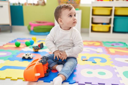 Foto de Adorable bebé caucásico jugando con el juguete del camión sentado en el suelo en el jardín de infantes - Imagen libre de derechos