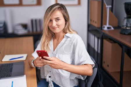 Téléchargez les photos : Jeune femme blonde travailleuse d'affaires utilisant un ordinateur portable et un smartphone au bureau - en image libre de droit