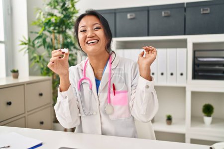 Photo for Young asian woman wearing doctor uniform and stethoscope celebrating victory with happy smile and winner expression with raised hands - Royalty Free Image
