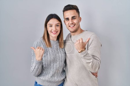 Téléchargez les photos : Jeune couple hispanique debout sur fond blanc pointant vers le dos derrière avec la main et les pouces levés, souriant confiant - en image libre de droit