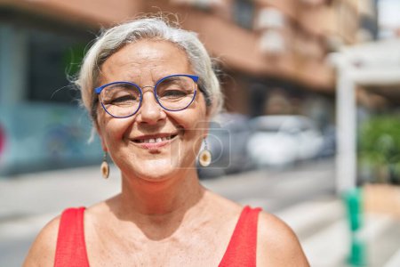 Foto de Mujer de pelo gris de mediana edad sonriendo confiada de pie en la calle - Imagen libre de derechos