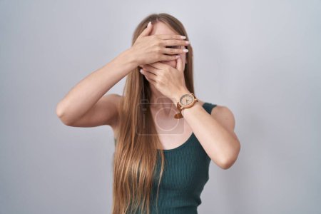 Téléchargez les photos : Young caucasian woman standing over white background covering eyes and mouth with hands, surprised and shocked. hiding emotion - en image libre de droit