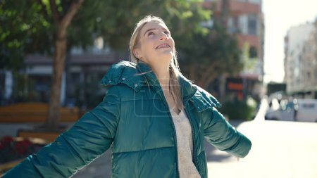 Foto de Joven mujer rubia sonriendo feliz con los brazos abiertos en el parque - Imagen libre de derechos
