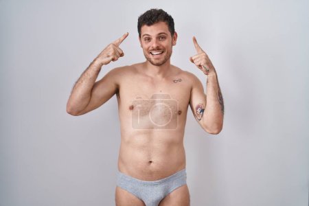 Foto de Young hispanic man standing shirtless wearing underware smiling pointing to head with both hands finger, great idea or thought, good memory - Imagen libre de derechos
