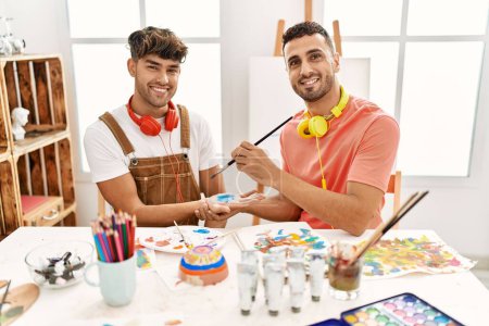 Photo for Two hispanic men couple smiling confident painting palm hands at art studio - Royalty Free Image