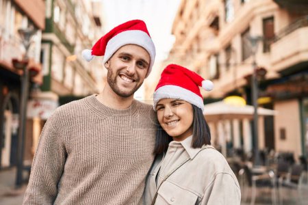Photo for Man and woman couple wearing christmas hat hugging each other at street - Royalty Free Image