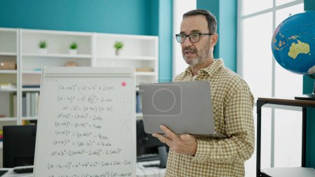 Téléchargez les photos : Middle age man teacher teaching lesson using laptop at classroom - en image libre de droit