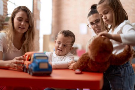 Téléchargez les photos : Professeurs avec garçon et fille jouant avec des voitures jouet et poupée assis sur la table à la maternelle - en image libre de droit