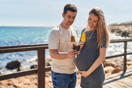 Photo for Man and woman couple expecting baby using smartphone at seaside - Royalty Free Image