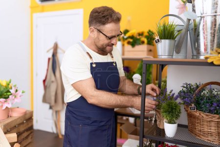 Foto de Hombre de mediana edad florista sonriendo confiado tocando planta de lavanda en la tienda de flores - Imagen libre de derechos