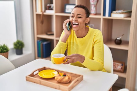 Téléchargez les photos : African american woman having breakfast talking on smartphone at home - en image libre de droit
