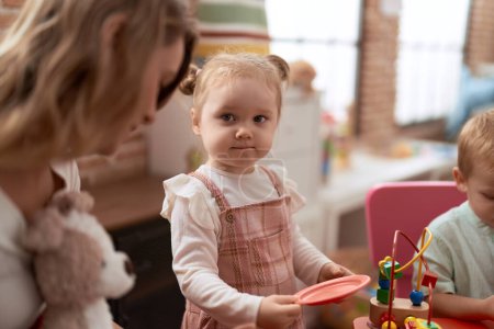 Foto de Profesor con niño y niña jugando con juguetes sentados en la mesa en el jardín de infantes - Imagen libre de derechos