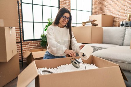 Photo for Young hispanic woman smiling confident unpacking cardboard box at new home - Royalty Free Image