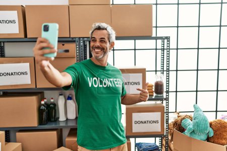 Téléchargez les photos : Middle age grey-haired man volunteer smiling confident make selfie by smartphone at charity center - en image libre de droit