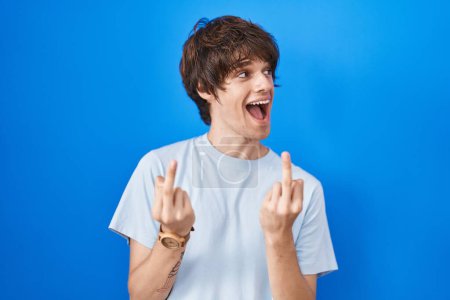 Foto de Hispanic young man standing over blue background showing middle finger doing fuck you bad expression, provocation and rude attitude. screaming excited - Imagen libre de derechos