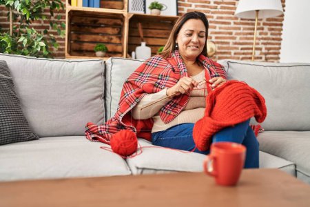 Photo for Middle age hispanic woman covering with blanket sewing at home - Royalty Free Image