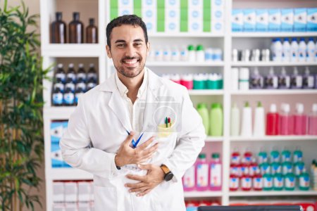 Photo for Handsome hispanic man working at pharmacy drugstore smiling and laughing hard out loud because funny crazy joke with hands on body. - Royalty Free Image