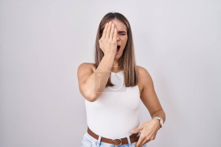 Foto de Hispanic young woman standing over white background yawning tired covering half face, eye and mouth with hand. face hurts in pain. - Imagen libre de derechos