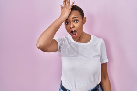 Photo for Beautiful african american woman standing over pink background surprised with hand on head for mistake, remember error. forgot, bad memory concept. - Royalty Free Image