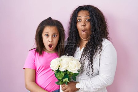 Photo for Mother and young daughter holding bouquet of white flowers afraid and shocked with surprise and amazed expression, fear and excited face. - Royalty Free Image
