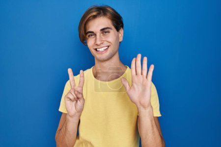 Téléchargez les photos : Jeune homme debout sur fond bleu montrant et pointant vers le haut avec les doigts numéro sept tout en souriant confiant et heureux. - en image libre de droit