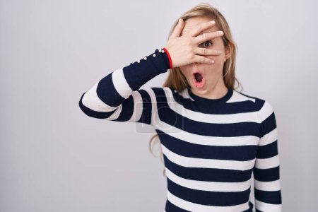 Foto de Mujer caucásica joven usando suéter azul marino casual asomándose en shock cubriendo la cara y los ojos con la mano, mirando a través de los dedos con expresión avergonzada. - Imagen libre de derechos