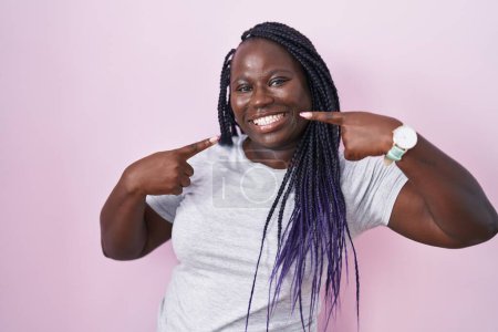 Photo for Young african woman standing over pink background smiling cheerful showing and pointing with fingers teeth and mouth. dental health concept. - Royalty Free Image