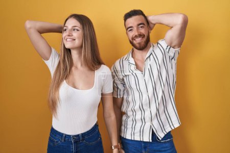 Photo for Young couple standing over yellow background smiling confident touching hair with hand up gesture, posing attractive and fashionable - Royalty Free Image