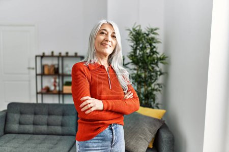 Téléchargez les photos : Femme aux cheveux gris d'âge moyen souriant confiant debout avec les bras croisés geste à la maison - en image libre de droit