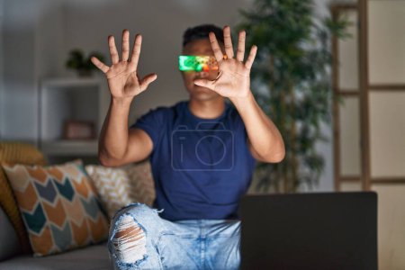 Téléchargez les photos : Young latin man using virtual reality glasses sitting on sofa at home - en image libre de droit