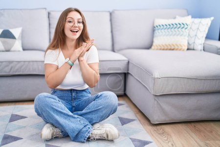 Photo for Young caucasian woman sitting on the floor at the living room clapping and applauding happy and joyful, smiling proud hands together - Royalty Free Image