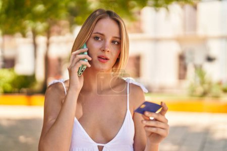 Téléchargez les photos : Jeune femme blonde parlant sur le smartphone et utilisant une carte de crédit au parc - en image libre de droit