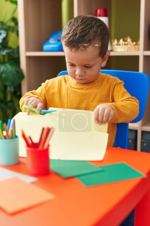 Photo for Adorable caucasian boy student cutting paper sitting on table at kindergarten - Royalty Free Image