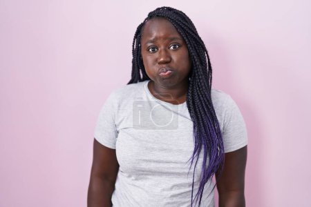 Téléchargez les photos : Jeune femme africaine debout sur fond rose joues gonflées avec un visage drôle. bouche gonflée d'air, expression folle. - en image libre de droit