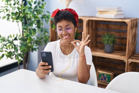 Téléchargez les photos : Jeune femme afro-américaine faire appel vidéo avec smartphone faire ok signe avec les doigts, sourire geste amical excellent symbole - en image libre de droit
