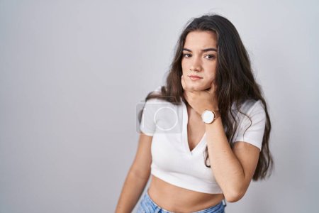 Téléchargez les photos : Jeune adolescente debout sur fond blanc touchant le cou douloureux, mal de gorge pour la grippe, la motte et l'infection - en image libre de droit