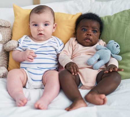 Foto de Dos bebés adorables sentados en la cama en el dormitorio - Imagen libre de derechos