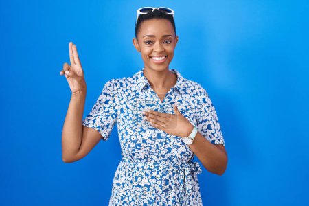 Photo for African american woman standing over blue background smiling swearing with hand on chest and fingers up, making a loyalty promise oath - Royalty Free Image