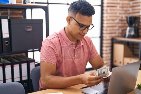 Téléchargez les photos : Young latin man business worker using laptop counting dollars at office - en image libre de droit