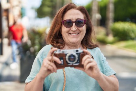 Foto de Senior woman tourist smiling confident holding camera at street - Imagen libre de derechos