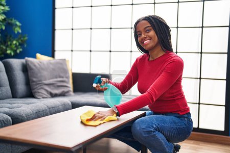 Téléchargez les photos : African american woman smiling confident cleaning table at home - en image libre de droit
