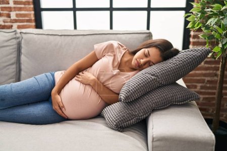 Foto de Mujer latina joven embarazada durmiendo en el sofá en casa - Imagen libre de derechos