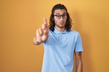Photo for Young hispanic man standing over yellow background pointing with finger up and angry expression, showing no gesture - Royalty Free Image