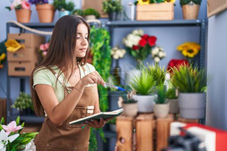 Téléchargez les photos : Jeune belle hispanique femme fleuriste lecture carnet à la boutique de fleurs - en image libre de droit