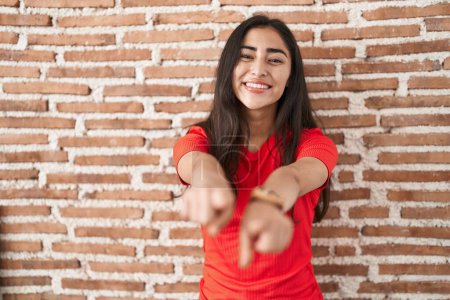 Photo for Young teenager girl standing over bricks wall pointing to you and the camera with fingers, smiling positive and cheerful - Royalty Free Image
