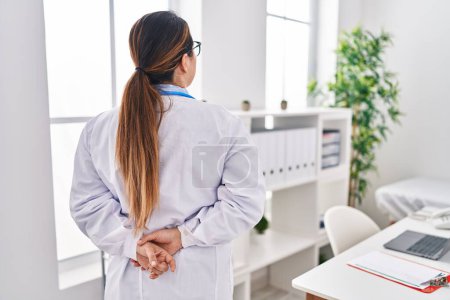 Photo for Young beautiful hispanic woman doctor standing on back view at clinic - Royalty Free Image